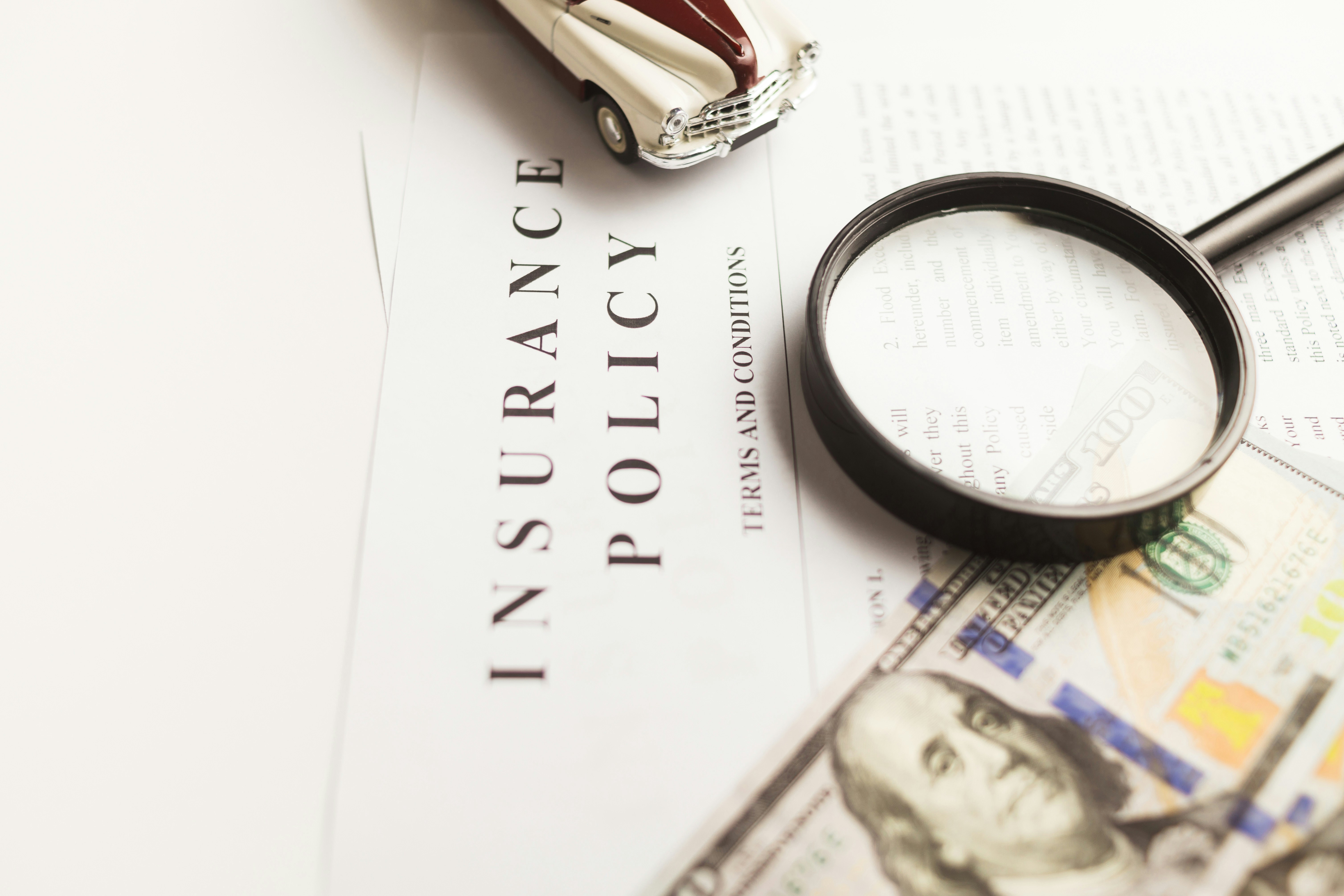 Insurance policy sits on a desk with a magnifying glass and money.
